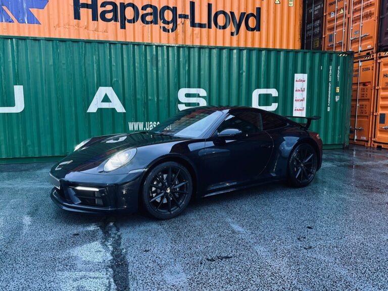 Porsche 911 in Schwarz, Heckansicht schräg rechts, vor Hapag-Lloyd Containern